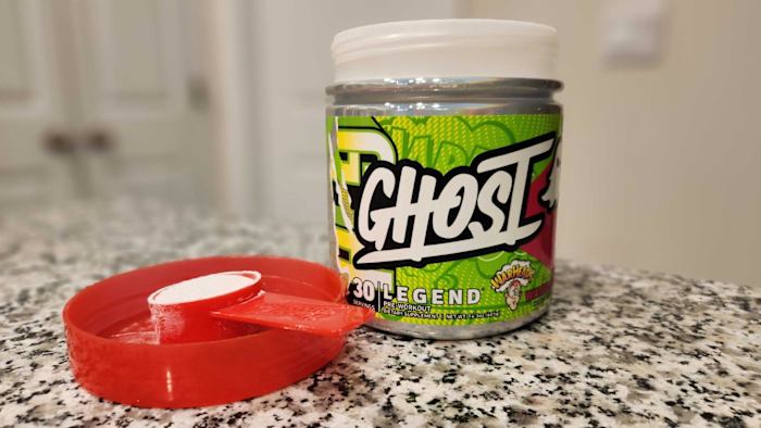 A green and red container of Ghost Legend pre-workout powder in Sour Watermelon Warhead flavor on a kitchen counter